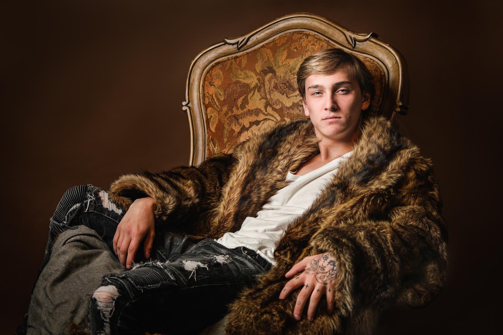 senior portrait of young man in a fur coat in a throne