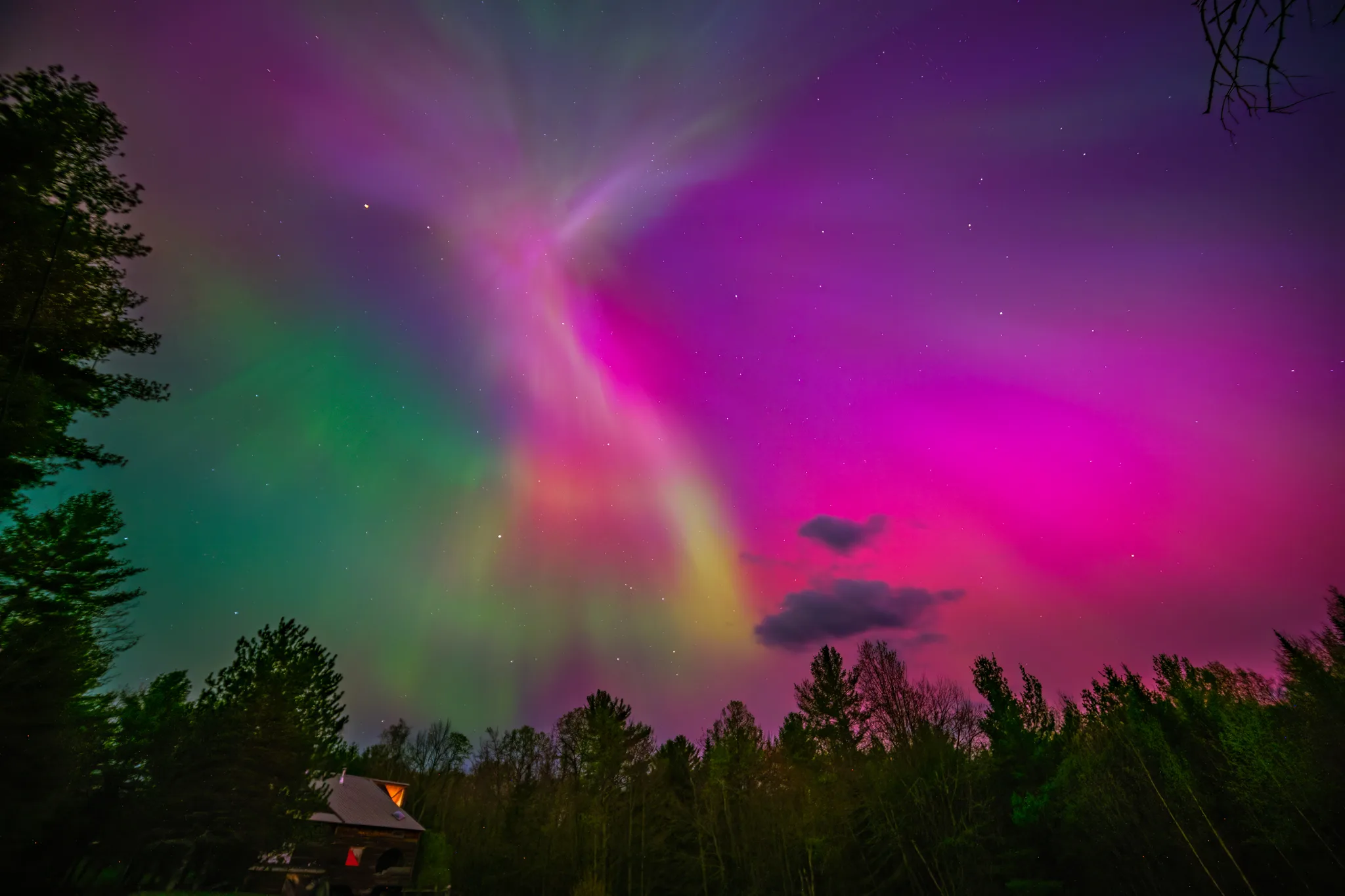 a colorful sky with trees and a house and the northern lights